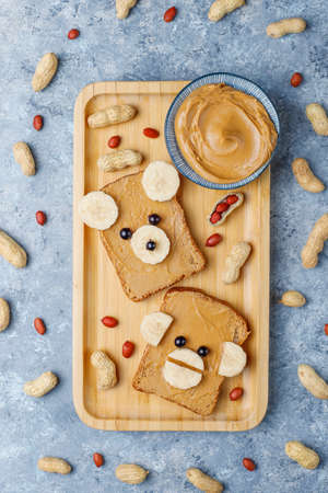 Funny bear and monkey face sandwich with peanut butter, banana and black currant,peanuts on grey concrete background,top viewの写真素材