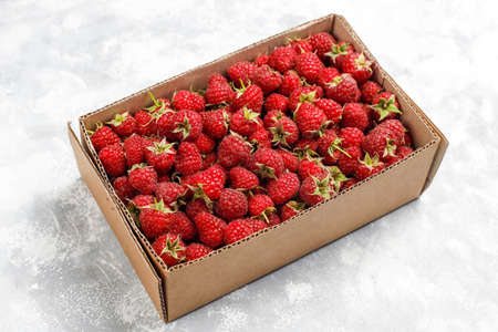 Ripe sweet raspberries in box on grey concrete background. Close up, top view