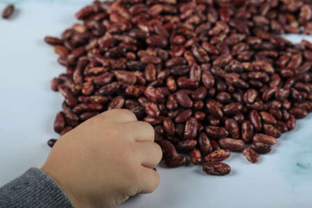 A kids hand taking red beans from the ground