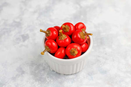Pickled small round red hot cherry chili peppers on grey concrete background