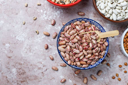Legumes and beans assortment in different bowls on light stone background . Top view. Healthy vegan...