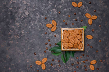 A cup of coffe with roasted coffee beans and coffe bean shaped cookies on dark background