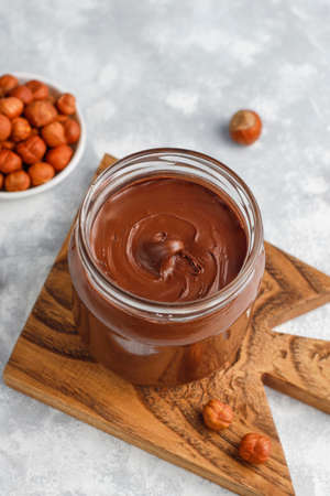 Chocolate spread or nougat cream with hazelnuts in glass jar on concrete background, copy space