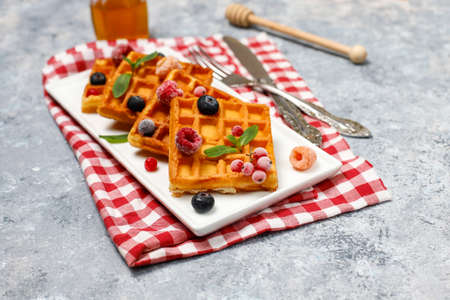 Traditional belgian waffles with fresh berries and honey on grey concrete background. Flat lay, top...