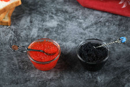 Black and red caviar, seafood in a small jars with a spoon inside on a marble tableの写真素材