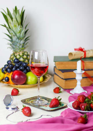 glass of rose wine on white wooden table with vintage books and clock,different tropical fruits and strawberriesの写真素材