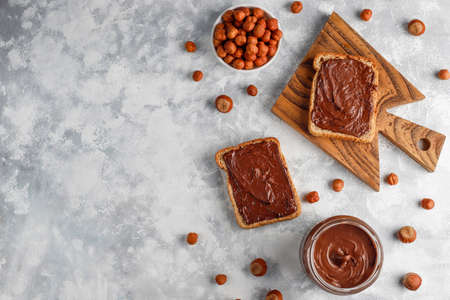 Chocolate spread or nougat cream with hazelnuts in glass jar on concrete background, copy space