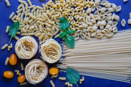 Italian food background. Italian cuisine. Ingredients tomatoes,yellow cherry tomatoes,fresh basil,black pepper corns,various pasta on dark background. Cooking concept. Cooking backgroundの写真素材