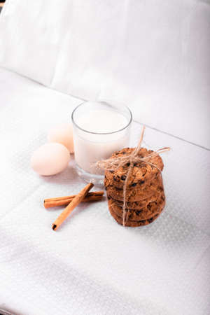 A glass of milk with caramel cookies, cinnamon sticks and raw eggs isolated on white