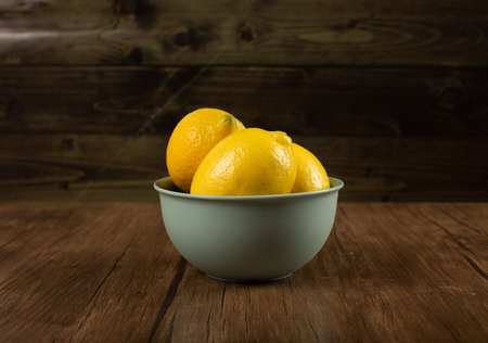 Yellow lemons in a bowl on wooden backgroundの写真素材
