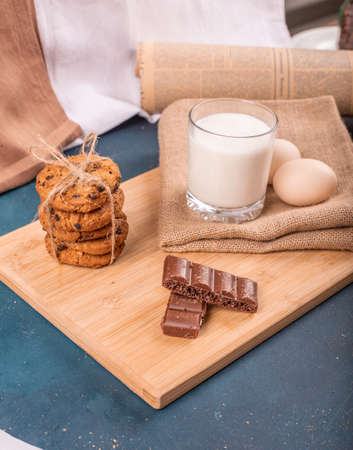 Chocolate pieces with oatmeal cookies and a book aside on a wooden platter