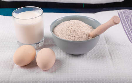A glass of milk with raw eggs and a bowl of all purpose flour