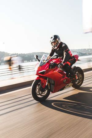A biker in gear and helmet biking a red motorcycle in the port