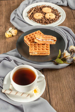 Cookies on coffee beans with waffler in a saucer and a cup of tea.