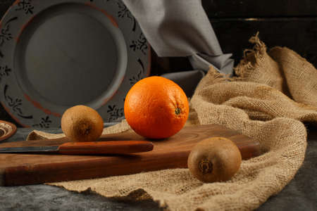 Orange and kiwies on a wooden board with a knife around.の写真素材