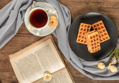 Waffles in a black saucer, a cup of tea and a book. top viewの写真素材