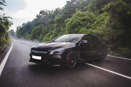 Black sedan parked in the middle of the forest road