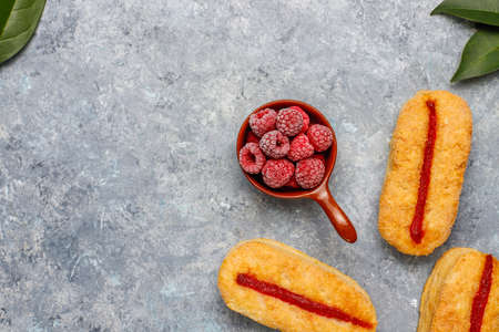 Puff pastry cookies with raspberry jam and frozen raspberries on light background