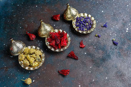 Assortment of dry tea in golden vintage mini plates.Tea types background:hibiscus,chamomile,mixed black tea,dry roses,butterfly pea teaの写真素材