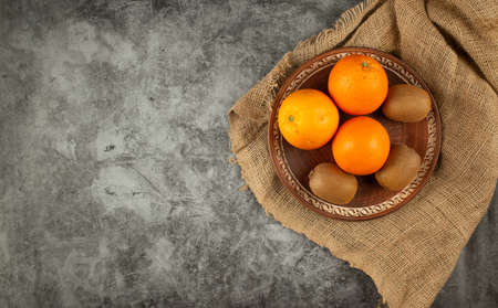 Orange and kiwies in a bowl on a burlap.