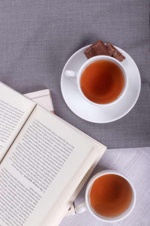 Book, cup of tea and chocolate on the tableの写真素材