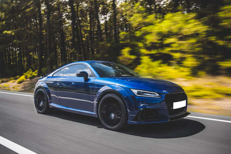 Blue luxury sedan coupe car on the highway in the forest