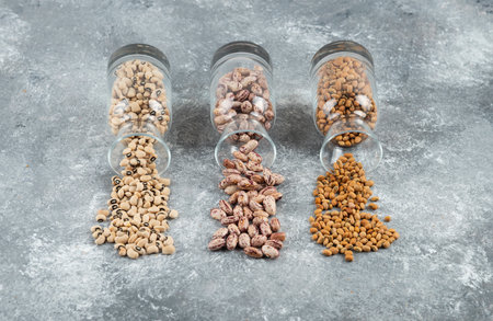 Three glasses of jar with unprepared beans on a gray background