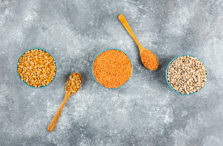 Three bowls of corn kernels, beans and red lentil on marble surfaceの写真素材