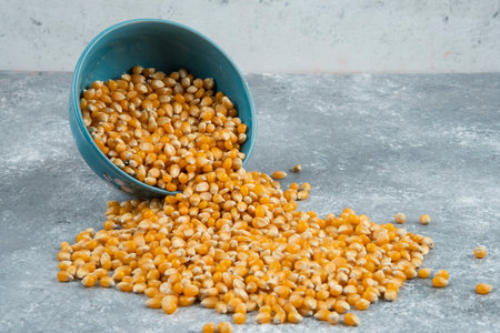 Raw corn kernels out of bowl on marble surface