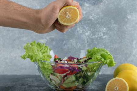 Close up photo.Man squeezing lemon to plate of mixed vegetable saladの写真素材