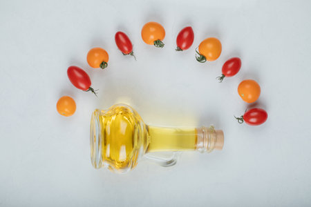 Gleaming red and yellow tomatoes on white background with bottle of oilの写真素材