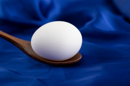 Single raw egg with wooden spoon on blue sateen cloth
