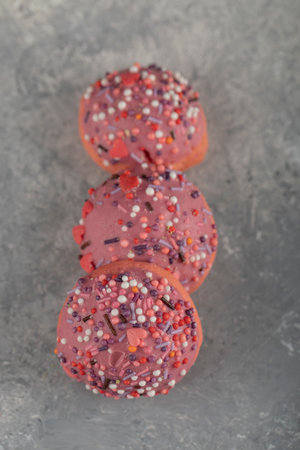 Three pink sweet doughnuts with sprinkles on dark backgroundの写真素材
