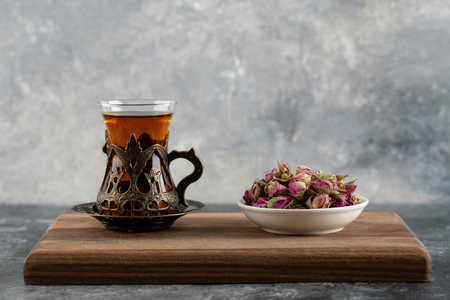 A glass cup of hot tea with dried roses on a wooden cutting boardの写真素材
