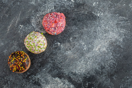 Three colorful sweet doughnuts with sprinkles on dark backgroundの写真素材
