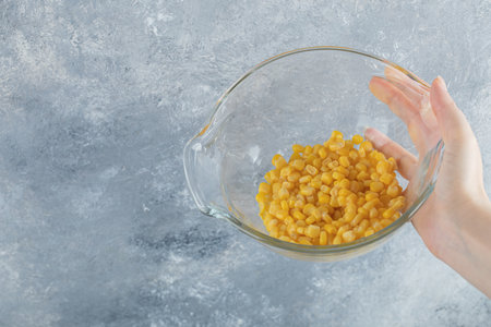 Female hand holding bowl of canned corns on marble backgroundの写真素材
