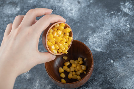 Hand adding popcorn seeds into a wooden bowl
