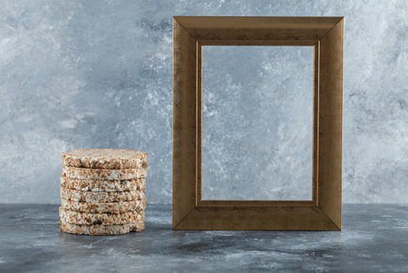 Stack of tasty crispbread with wooden empty frame on blue background