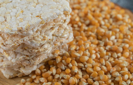 Stack of tasty crispbread and raw corns on blurry background