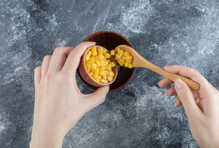 Hand adding popcorn seeds into a wooden bowl