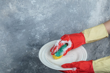 Hands in protective gloves washing plate with spongeの写真素材
