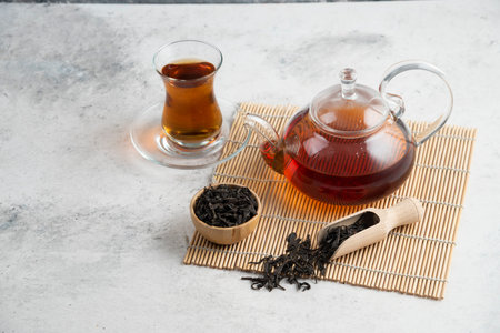 A glass cup of tea with dried loose teas and teapotの写真素材