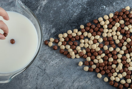 Hand adding cereal balls into bowl of milk on marble backgroundの写真素材