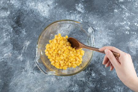 Female hand mixing sweet corns in glass bowl