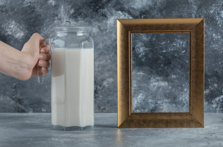 Female hand holding jug of milk on marble backgroundの写真素材