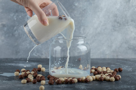 Female hand pouring fresh milk to jar with cereal ballsの写真素材