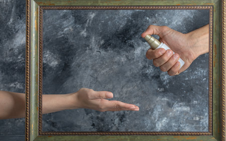 Male hand spraying ethanol to female in middle of frameの写真素材