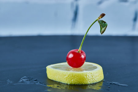 Juicy yellow lemon slice with a cherry on blue backgroundの写真素材