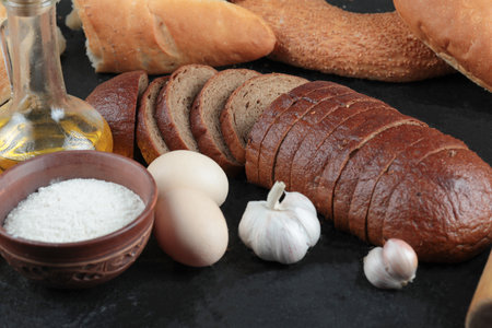 Whole and sliced bread, eggs, garlic, flour bowl and glass of oilの写真素材