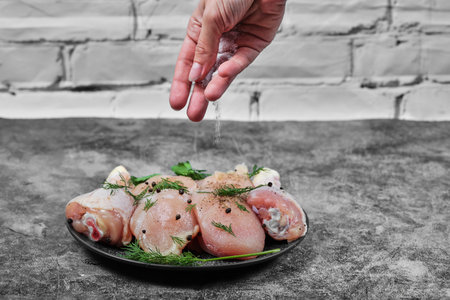 Woman adds spices to raw chicken meat slices on stone tableの写真素材